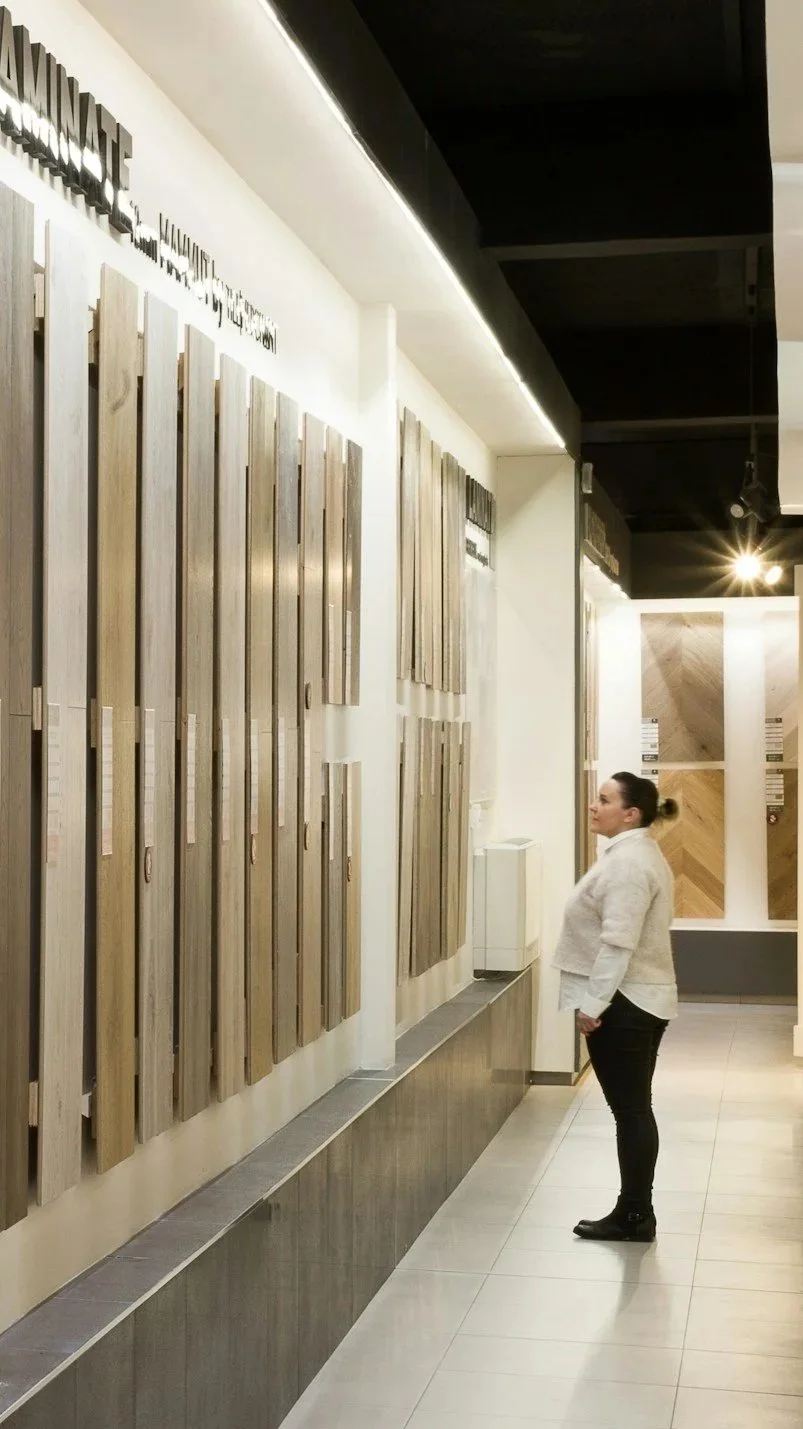 A woman shopping for wood samples in a flooring store, looking at various wooden floor swatches on the wall.