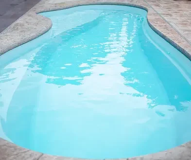 Empty swimming pool with clear blue water and a curved shape, surrounded by concrete decking.