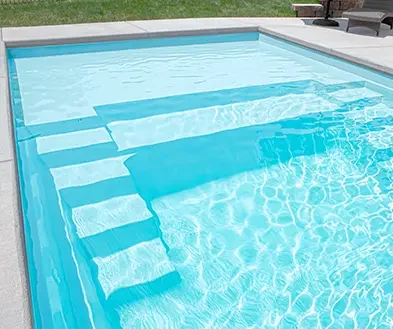 Inground swimming pool with steps leading into the water, surrounded by a concrete deck with outdoor furniture.