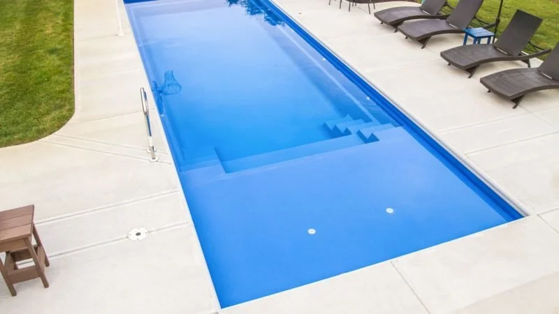 A backyard swimming pool with a cover on, surrounded by lounge chairs and a concrete patio.