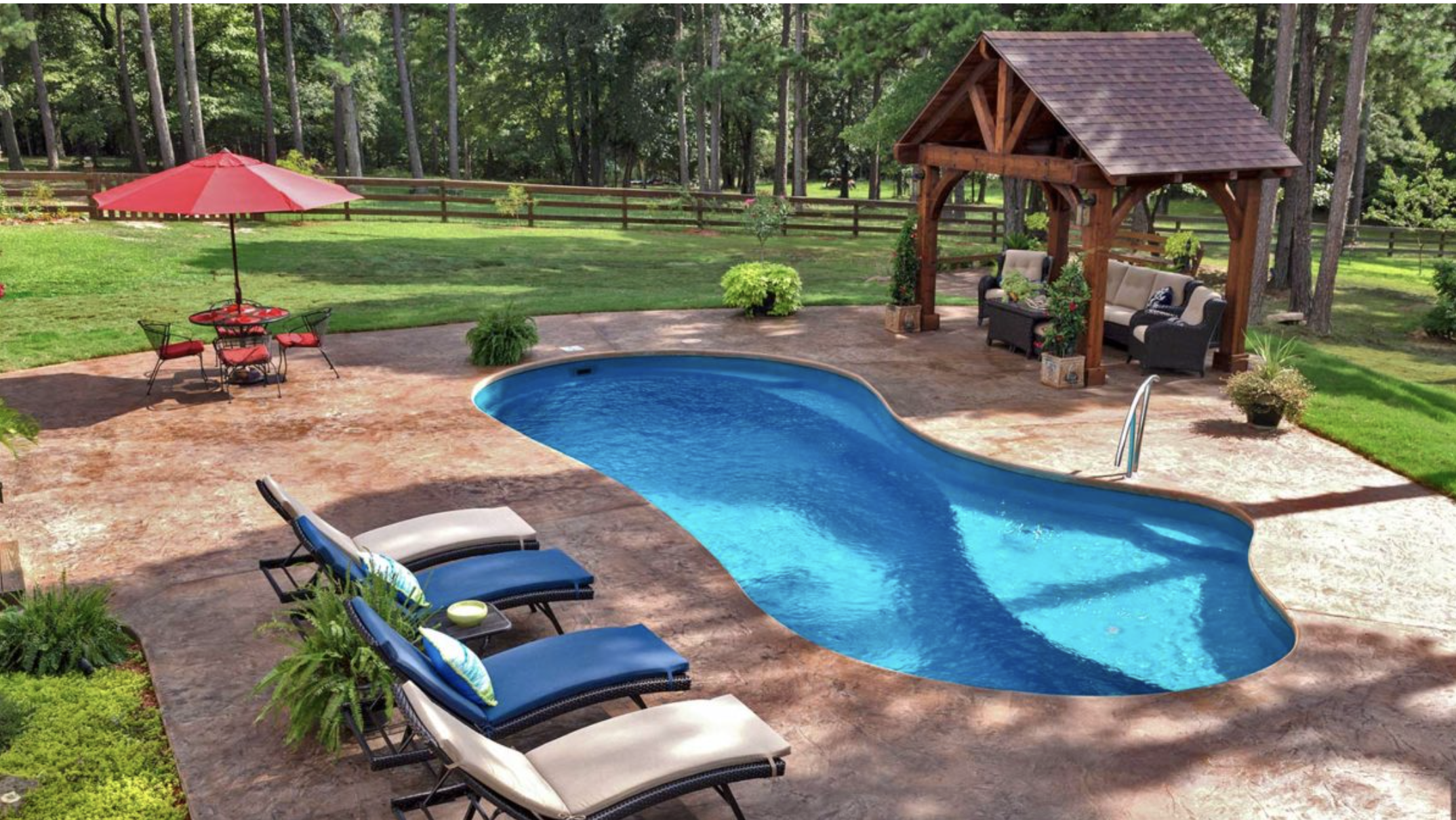 A backyard with a swimming pool, lounge chairs, a red patio umbrella, a wooden gazebo with outdoor seating, potted plants, and a grassy yard surrounded by trees.
