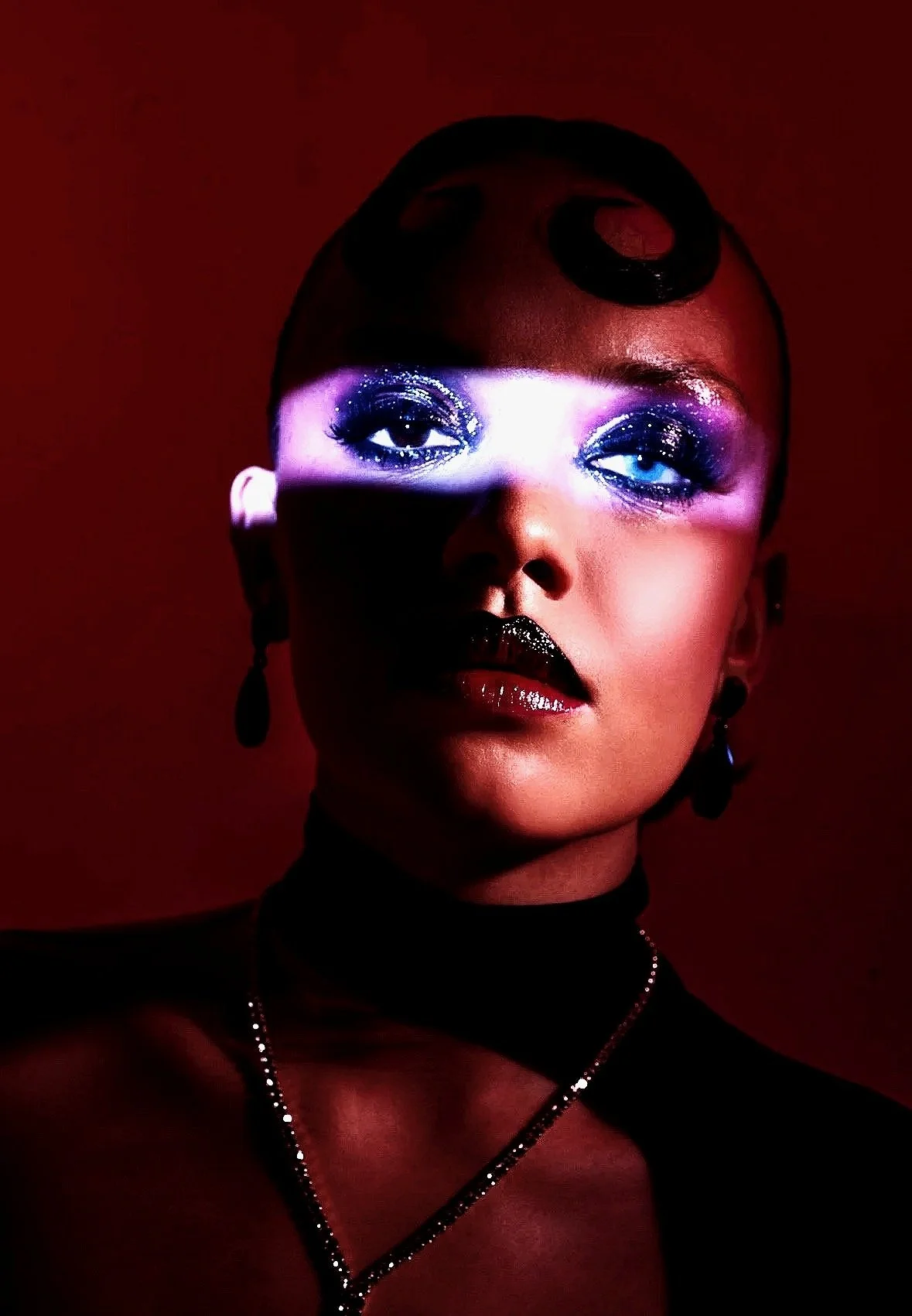 A woman with dark lipstick and glittery eye makeup, wearing earrings and a necklace, posed against a dark red background with dramatic lighting.