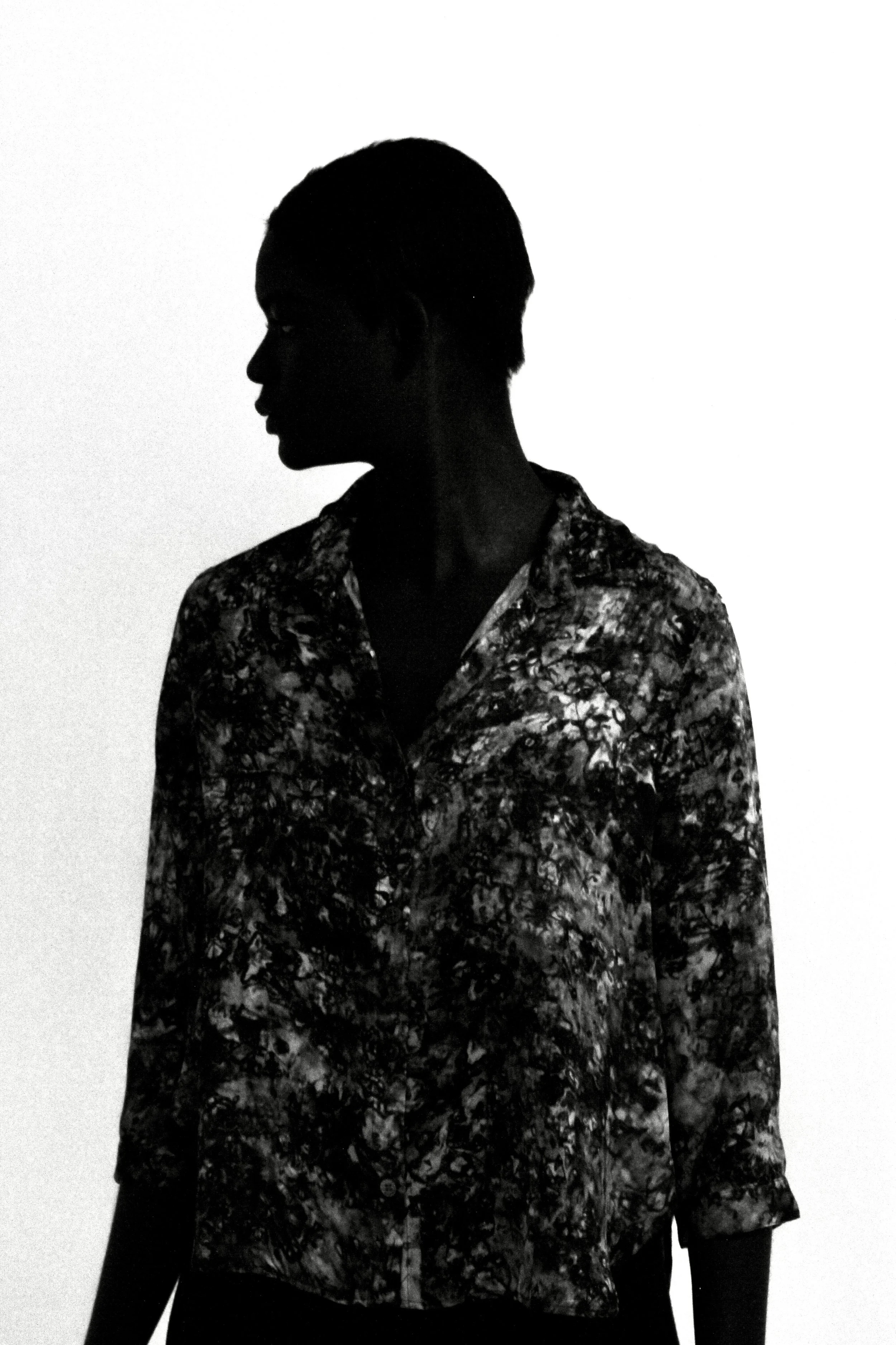 Silhouette of a person with short hair wearing a patterned shirt, standing against a plain background.