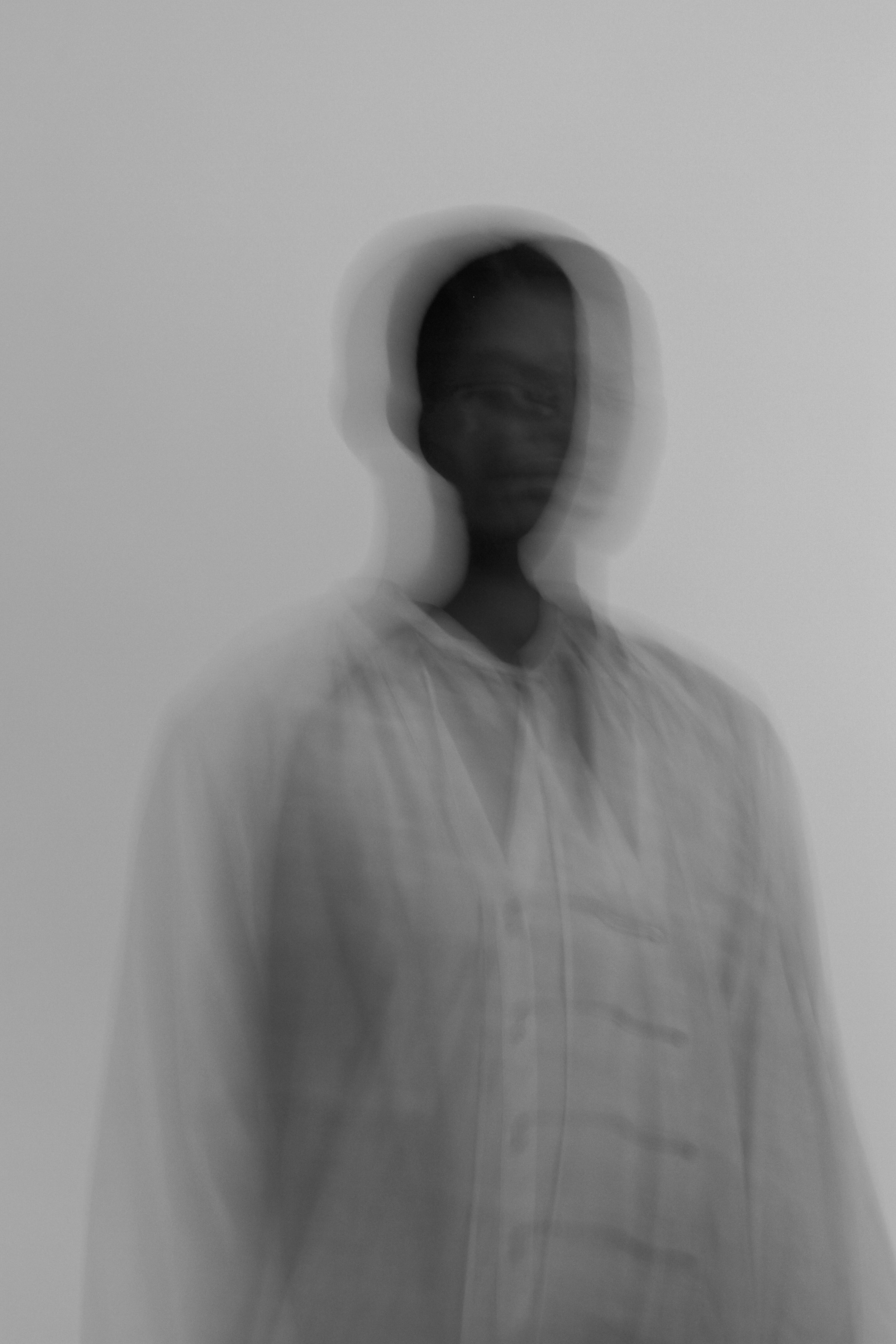 Black person with dark skin and short hair, wearing a light-colored shirt, standing in front of a plain background, with a blurry, double-exposure effect.