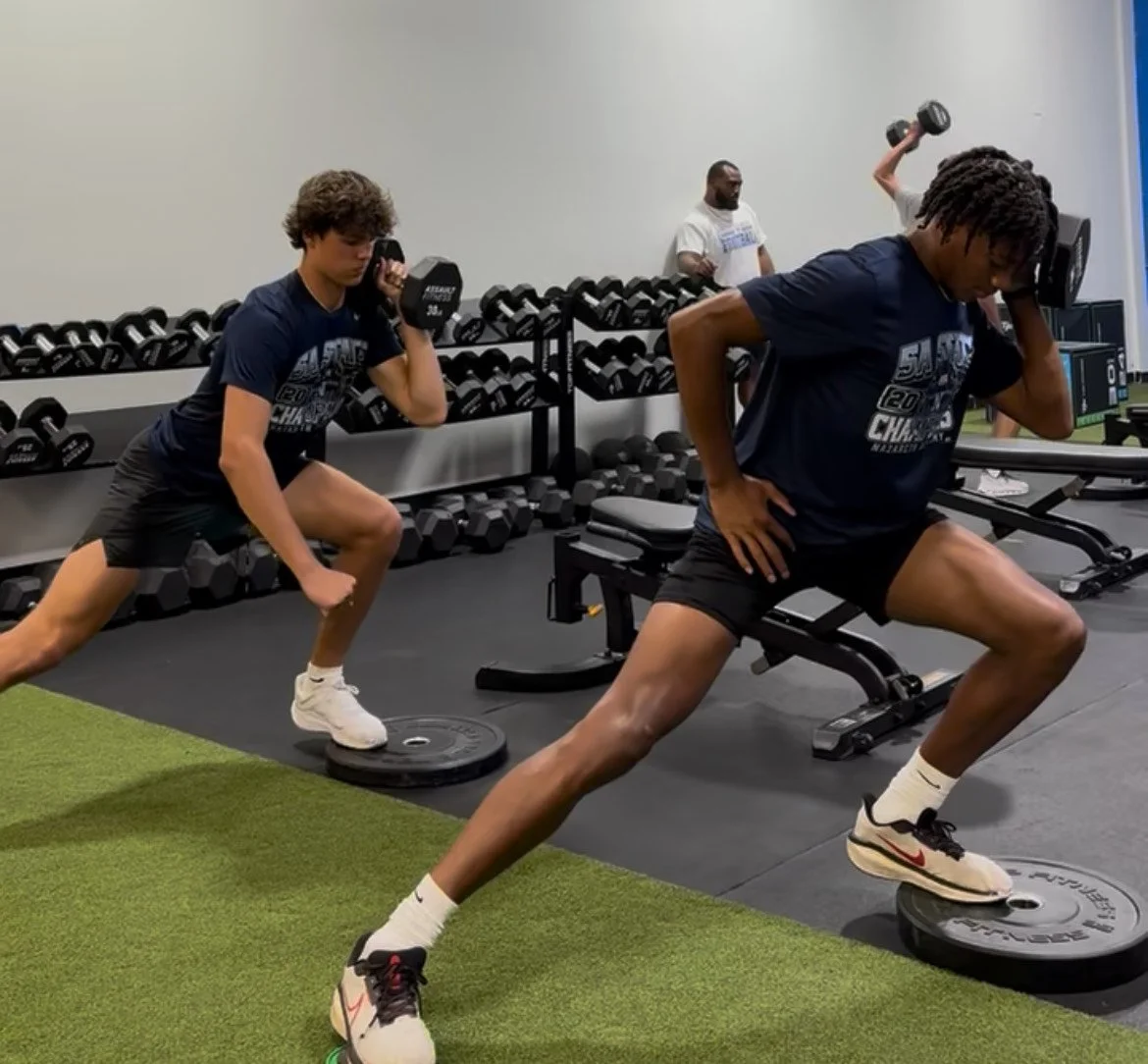 Young men exercising with dumbbells and weight plates in a gym.
