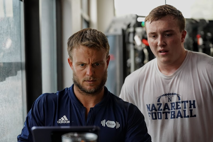 Two men look at a tablet screen in a gym or training facility.