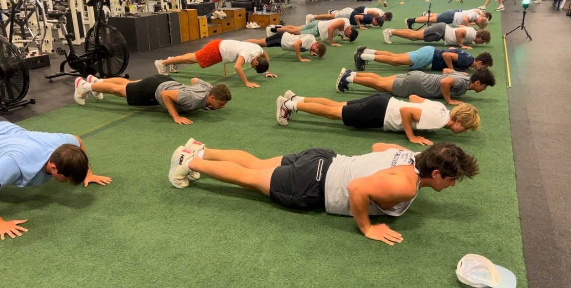 Group of people doing push-ups on a green gym floor in a fitness center.