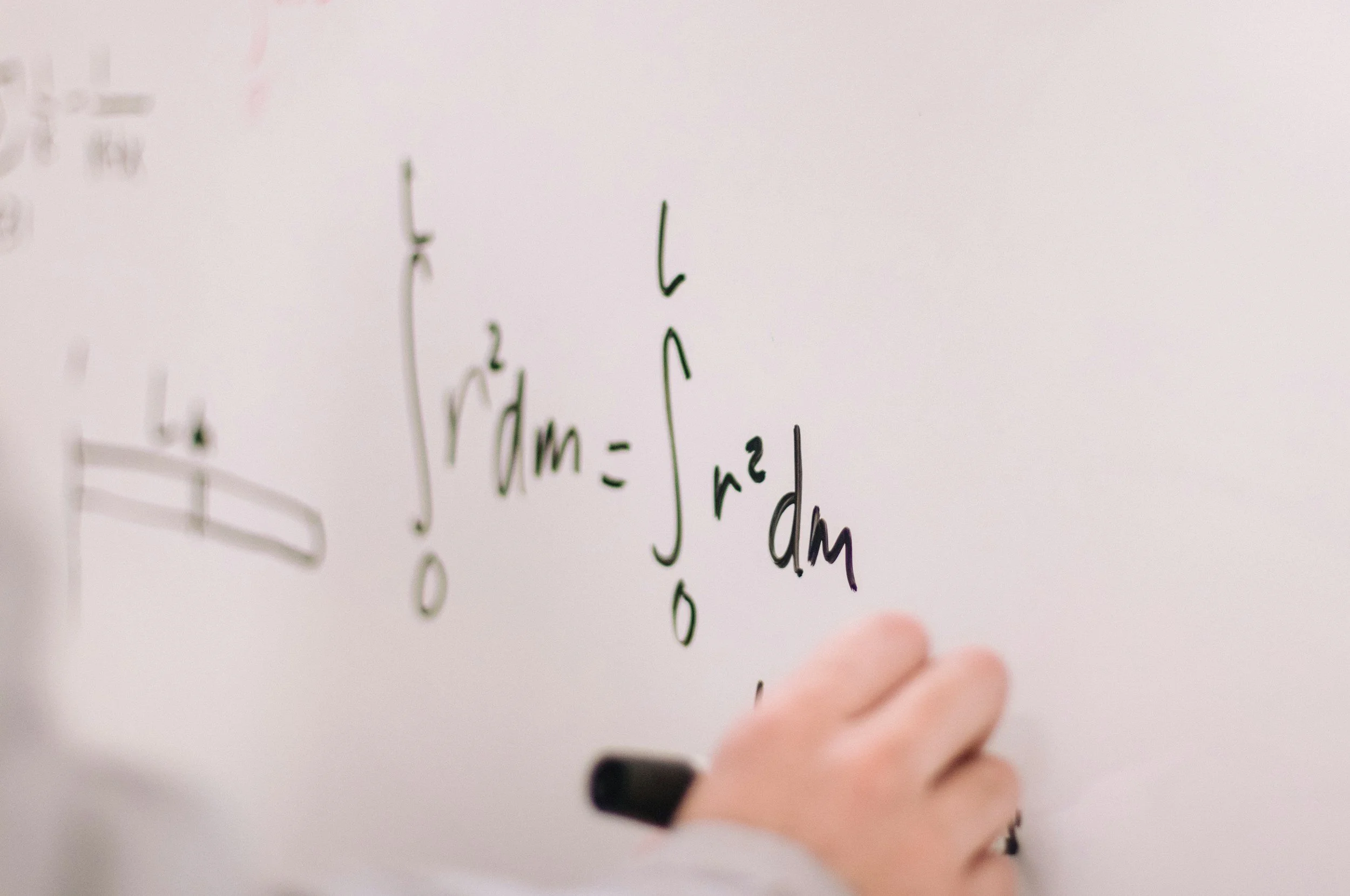A person writing a mathematical integral equation on a whiteboard with a black marker.