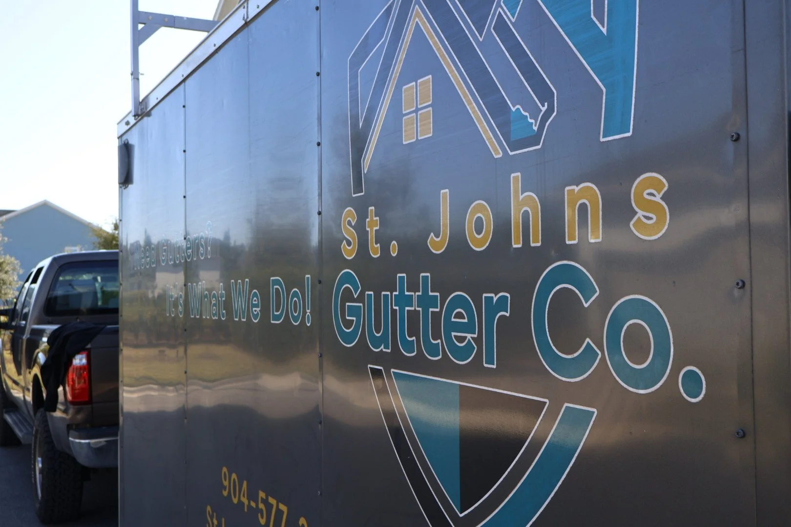 A business truck with a large sign advertising St. Johns Gutter Co. on the side, featuring a logo with a house and gutter illustration.