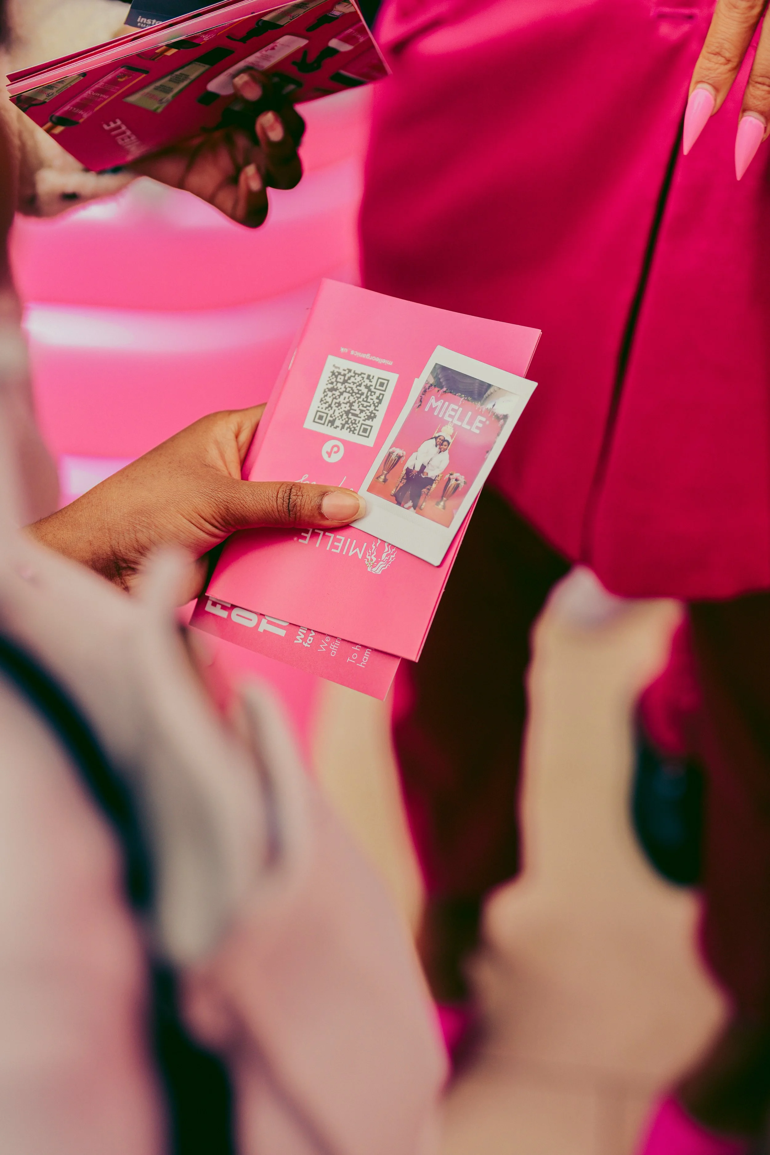 Close-up of two people exchanging pink event passes with a QR code and photo, with one person holding her phone.