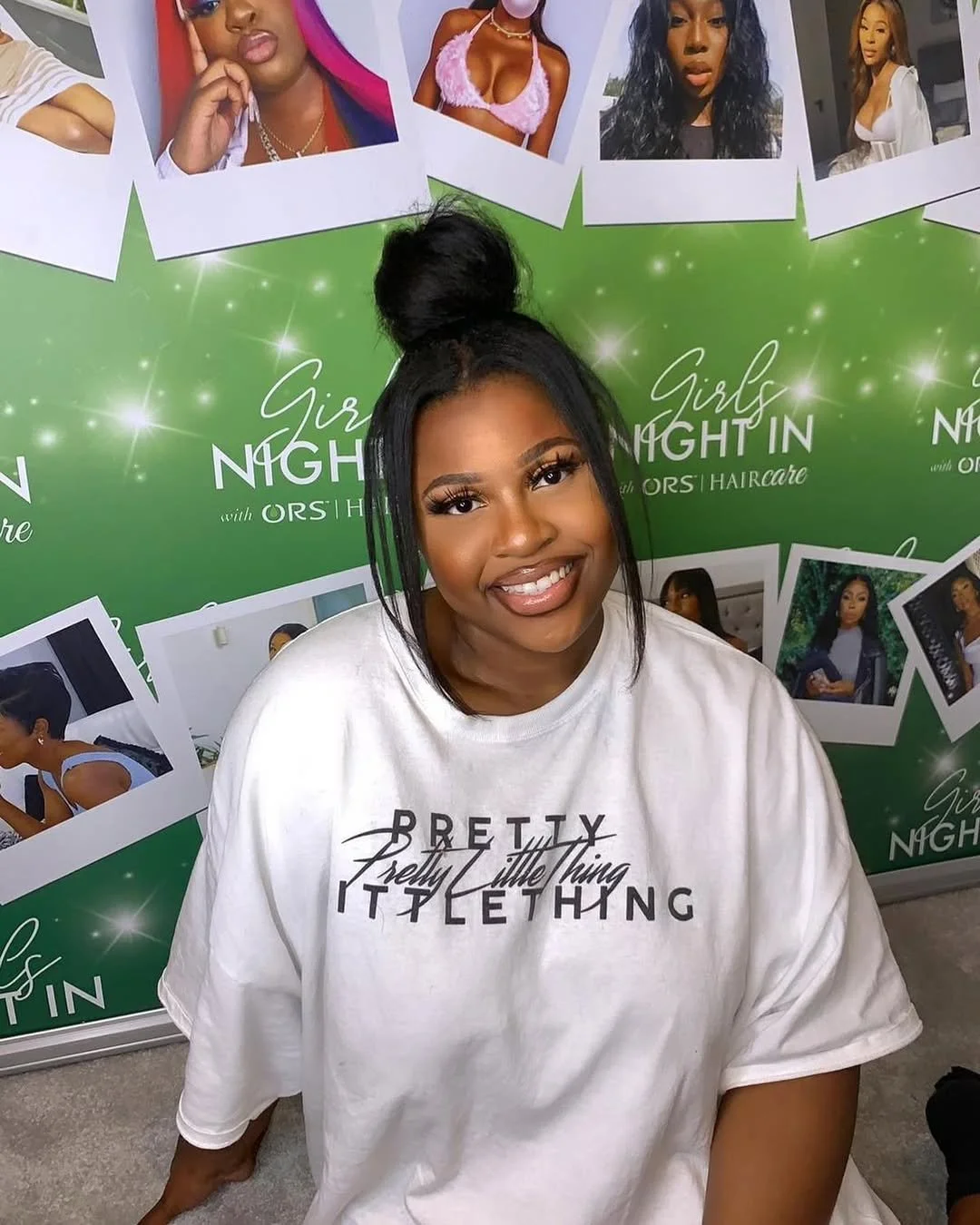 Smiling woman with dark hair styled in a high bun, wearing a white T-shirt and sitting in front of a green background with photos of women and the text 'Girls Night In with ORS Haircare'.