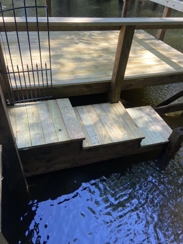 Wooden dock with steps leading down to the water and a small metal gate at the top of the stairs.