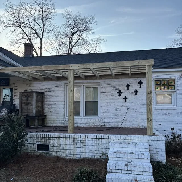 Backyard of a house with a newly constructed wooden porch with a roof, white brick steps, and black decorative crosses on the white brick wall.
