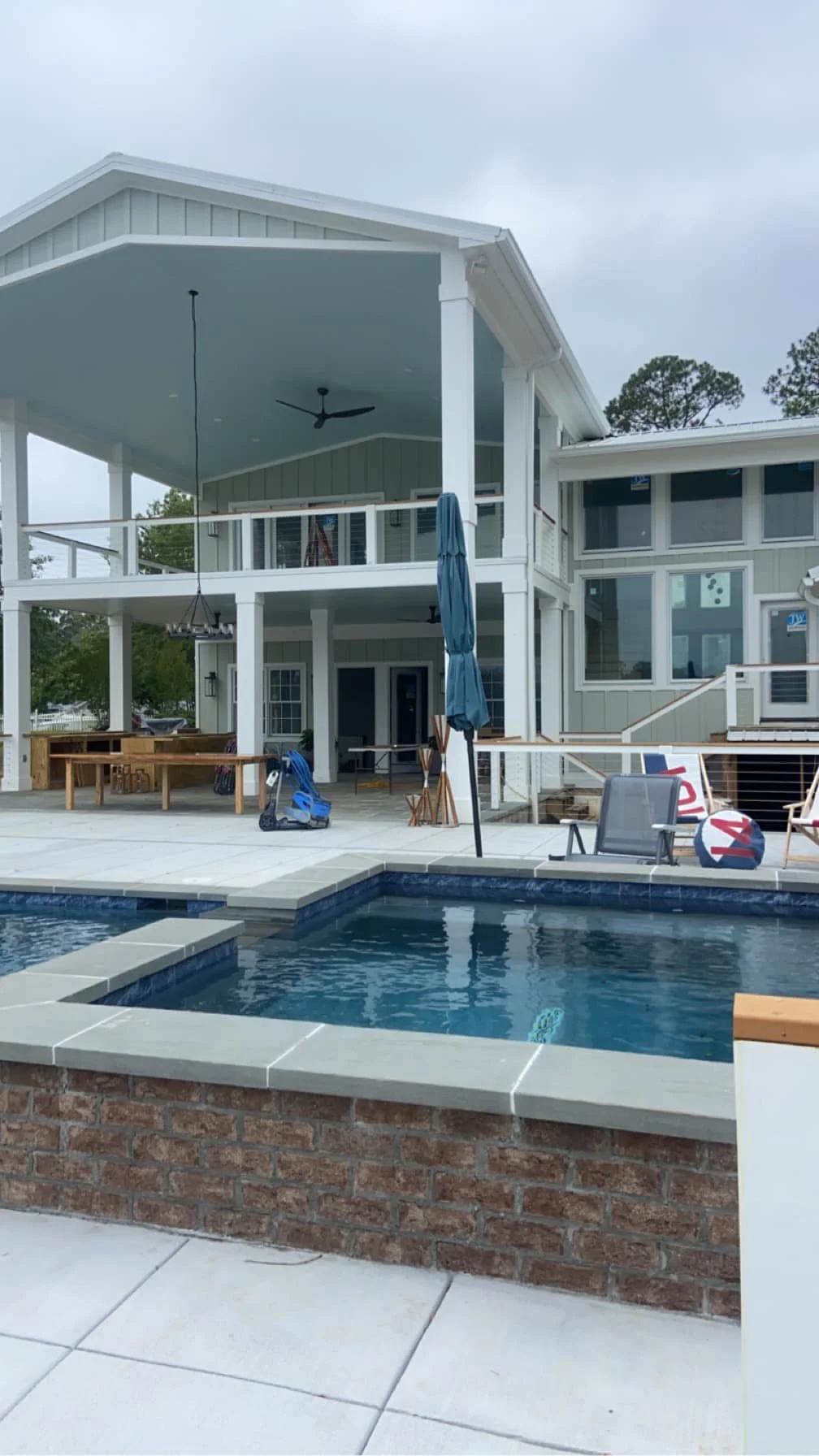 A backyard with a swimming pool in front of a two-story house with a covered balcony and large windows.