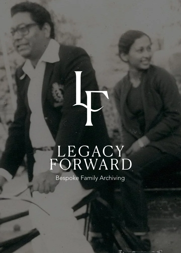 Black and white photo of a man and woman sitting outdoors, smiling. The man is wearing glasses, a suit jacket, and a white shirt, while the woman is dressed in a dark jacket. Overlaid text reads "Legacy Forward: Bespoke Family Archiving."