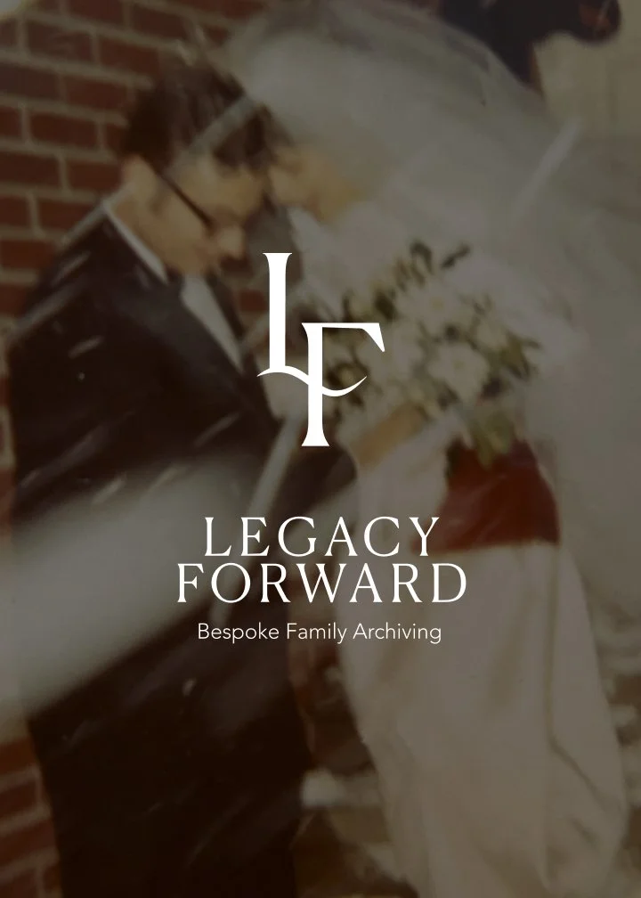 A person dressed in historical military uniform, wearing glasses and a white hat, holding a bouquet of white flowers, and standing against a brick wall.