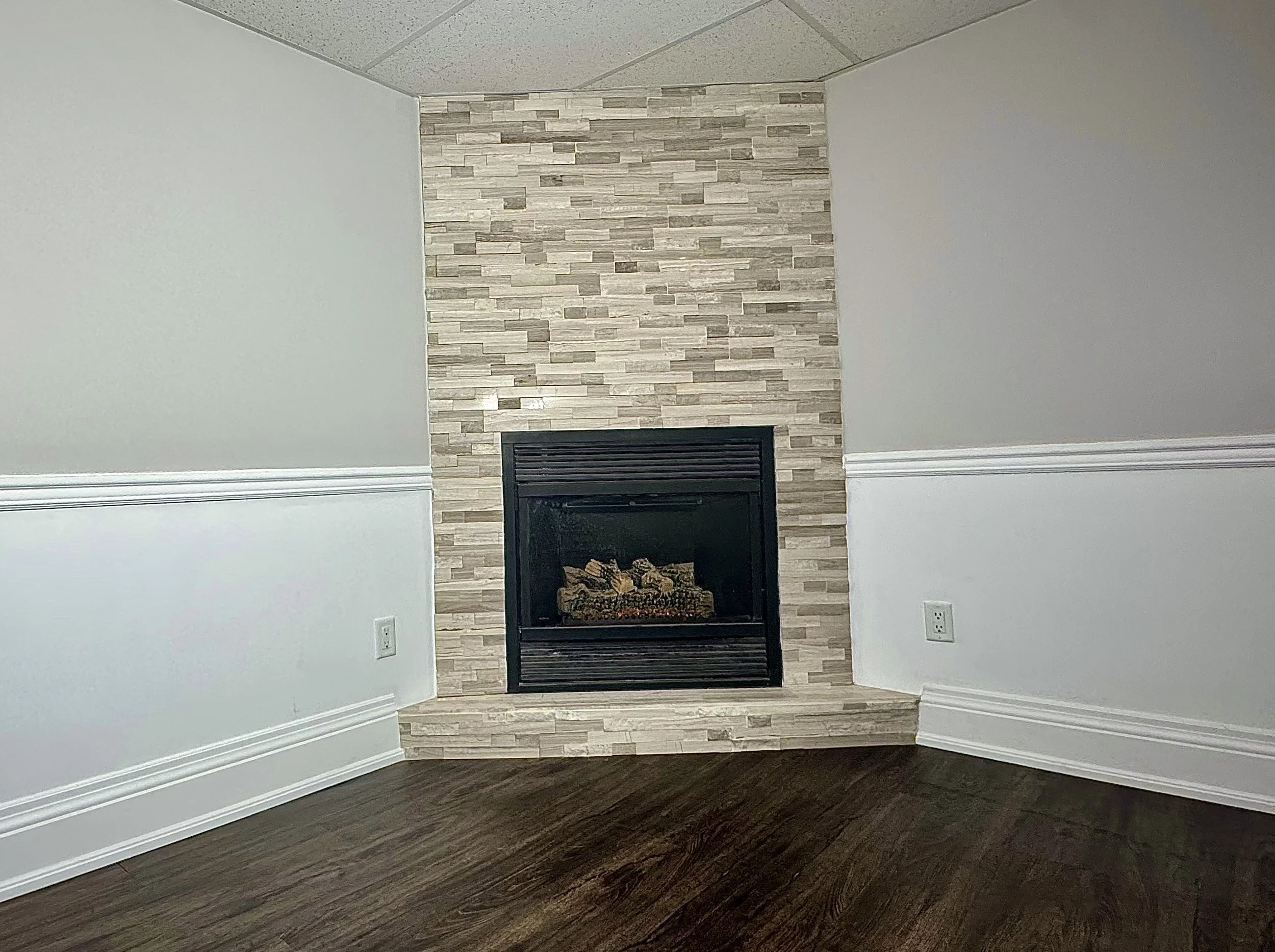 Basement fireplace feature wall with light stone tile dark floor and white wainscoting