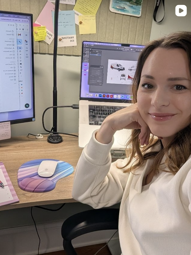 Harrisonburg designer, Vika Samoylov works at a desk with laptop and a branding project with truck wrap.