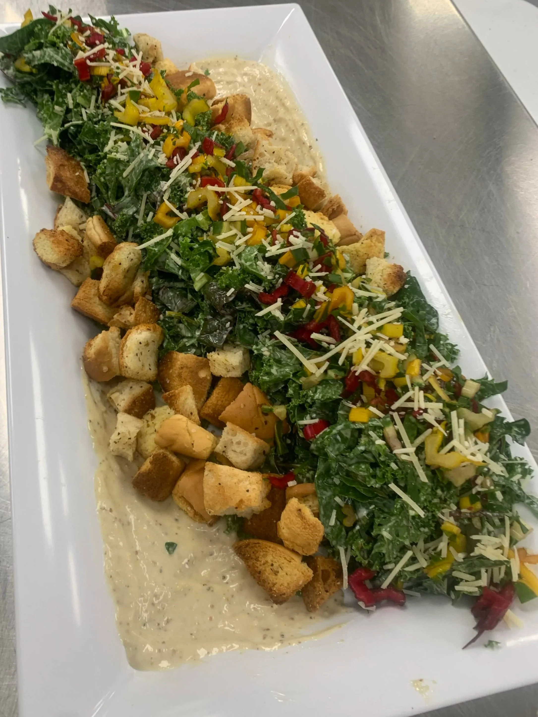 Caesar salad with croutons, shredded cheese, and chopped vegetables on a bed of greens, served with dressing.