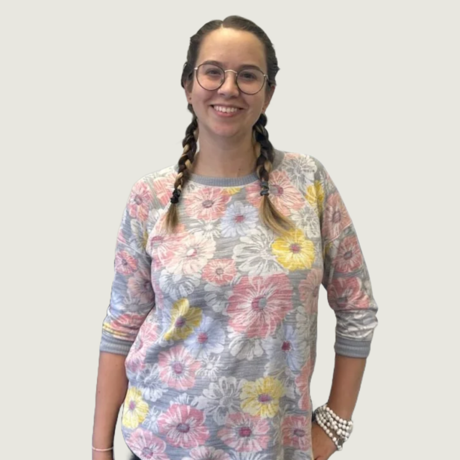 Smiling woman with glasses and braided hair wearing a floral long-sleeve shirt and jewelry.