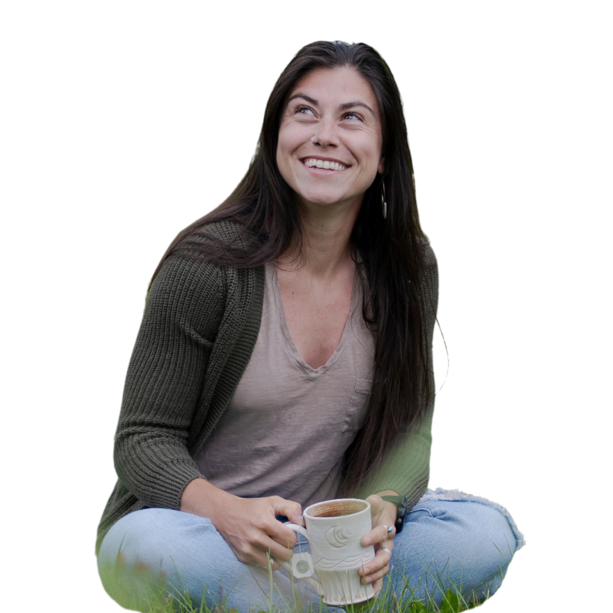 Young woman sitting on grass, holding a cup of coffee and smiling, with a peaceful outdoor background.