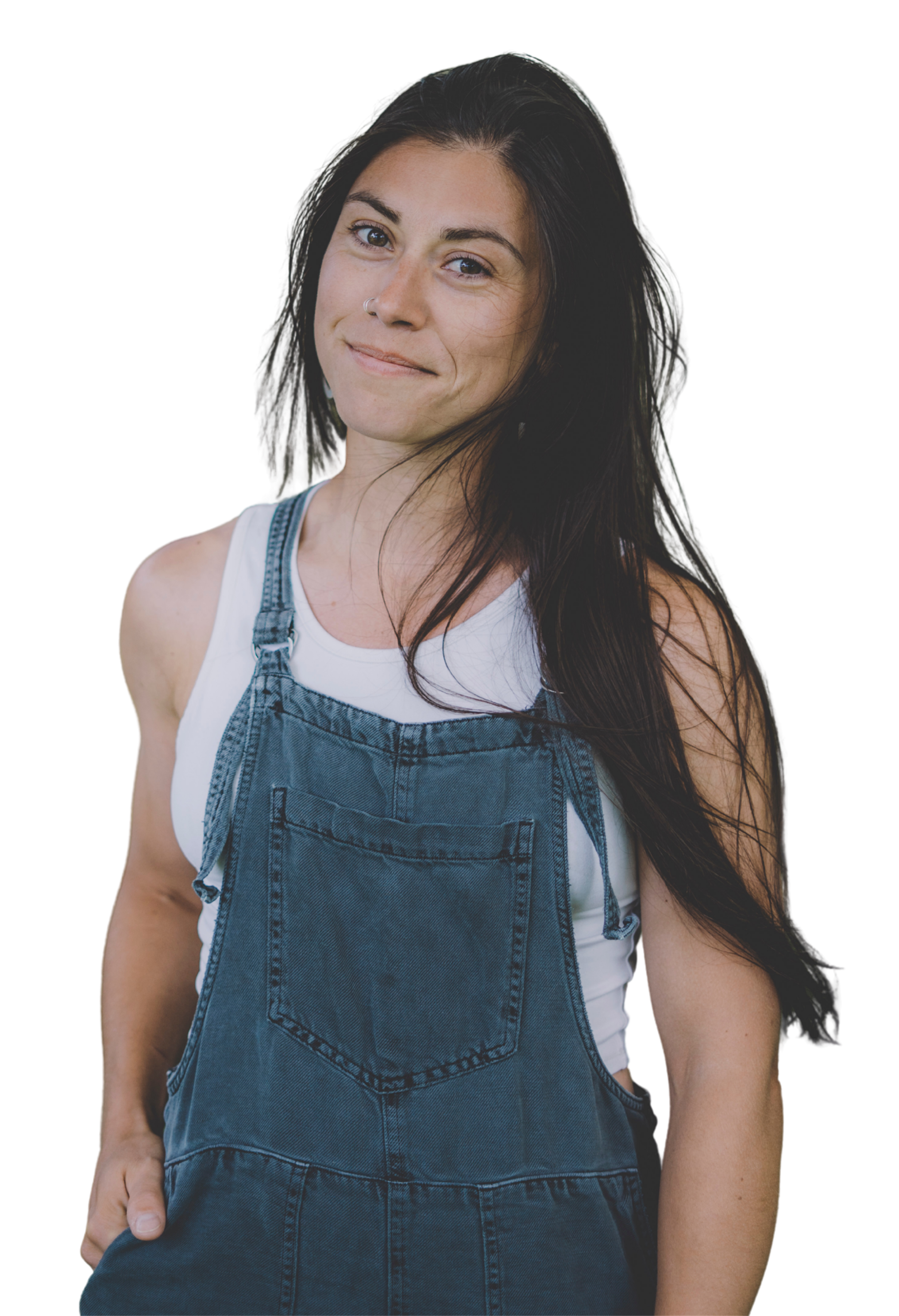 A woman with long dark hair, wearing a white shirt and denim overalls, standing against a black background.