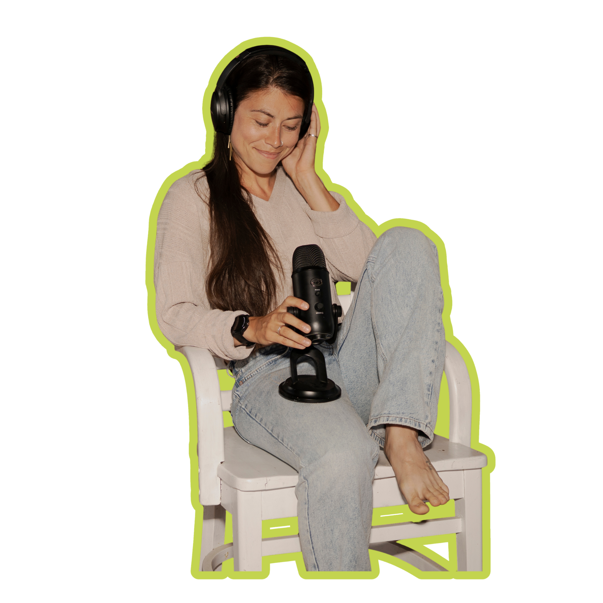 Woman sitting on a white wooden chair with her eyes closed, wearing headphones, holding a microphone, and smiling softly.