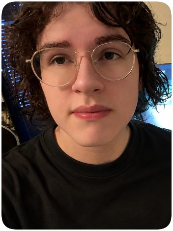 Close-up of a person with curly brown hair, glasses, and wearing a black shirt, indoors.