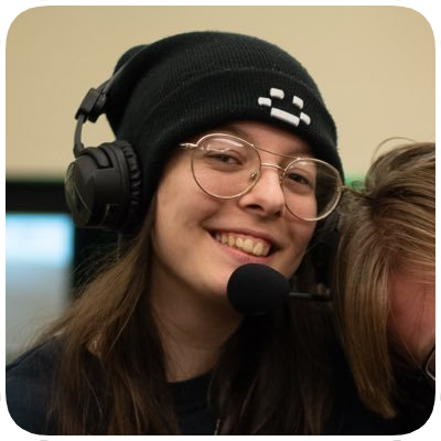 Young woman wearing glasses, a black beanie, and headphones, smiling at the camera.