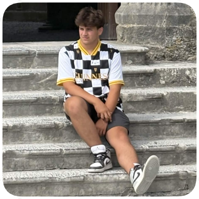 A young boy sitting on stone steps outside, wearing a black and white checkered shirt, shorts, and sneakers.