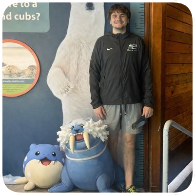 Young man standing next to life-sized Pokémon figures, including a Blastoise and Dugtrio, at an indoor exhibit.