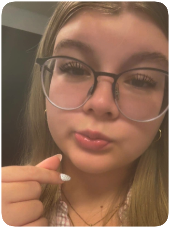 Close-up of a young woman with long hair wearing glasses, slightly pouty lips, holding her hand near her chin.