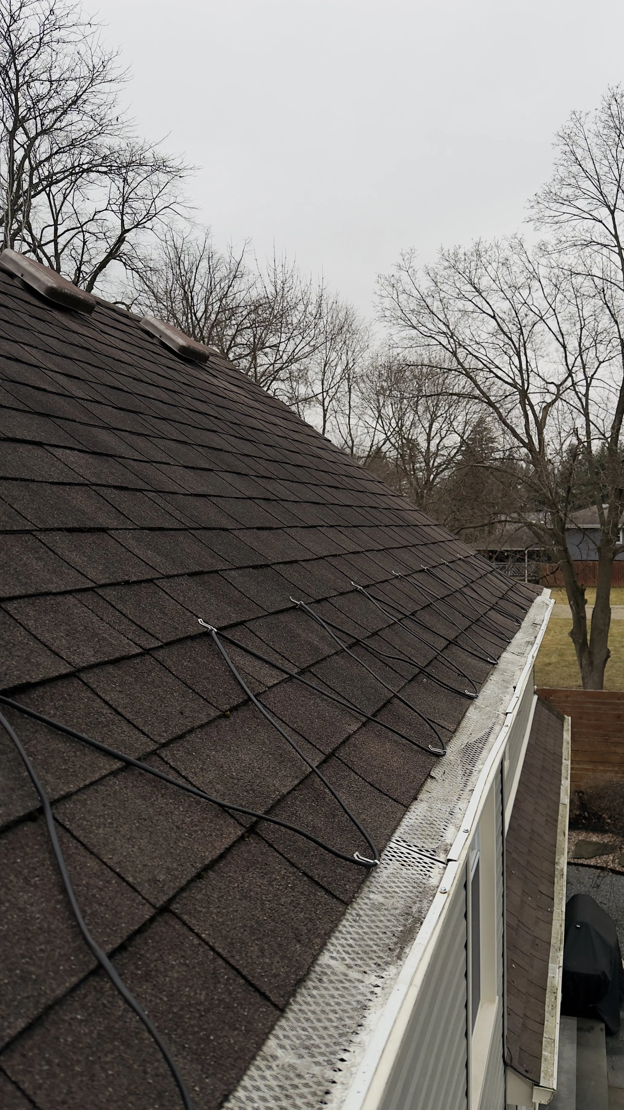 View of a house roof with cable wires installed along the shingle surface