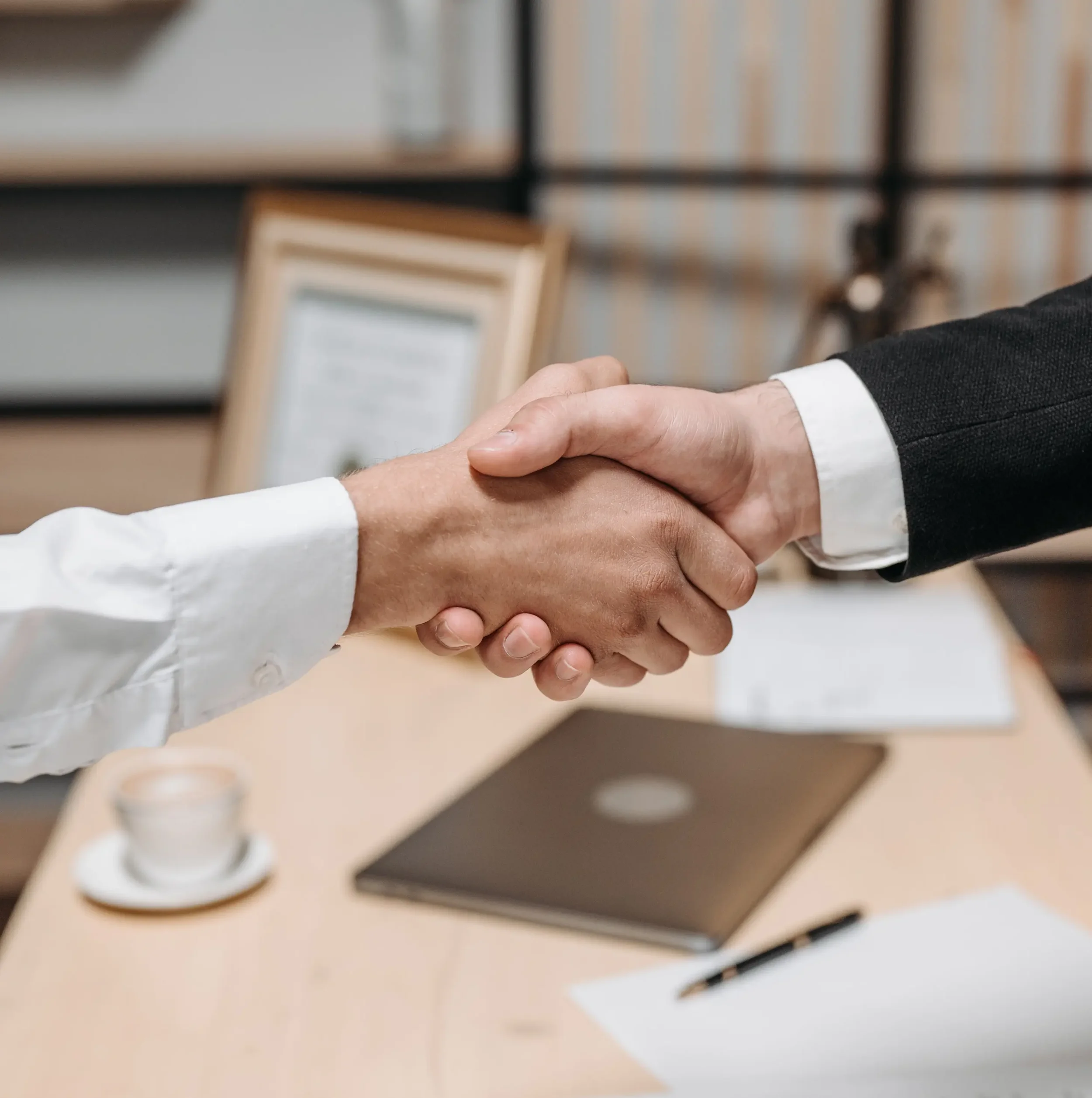 Close-up of two professional partners shaking hands over a desk during a meeting.