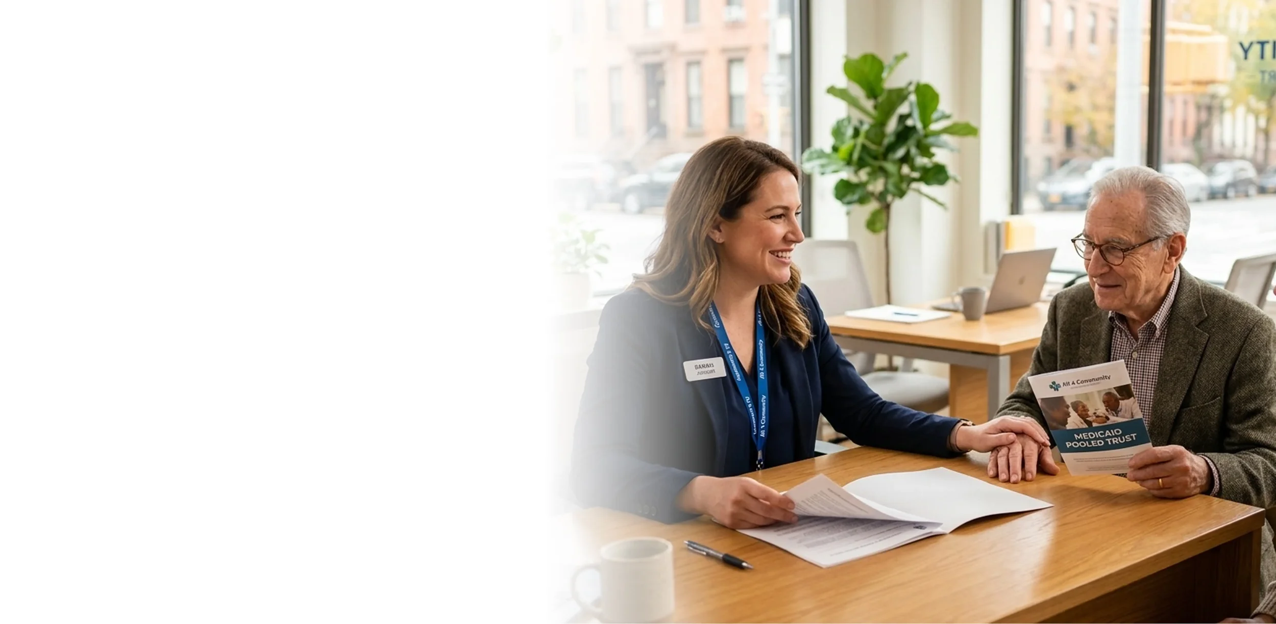 Care coordinator sitting at a desk and smiling while assisting a senior man holding a Medicaid Pooled Trust brochure.