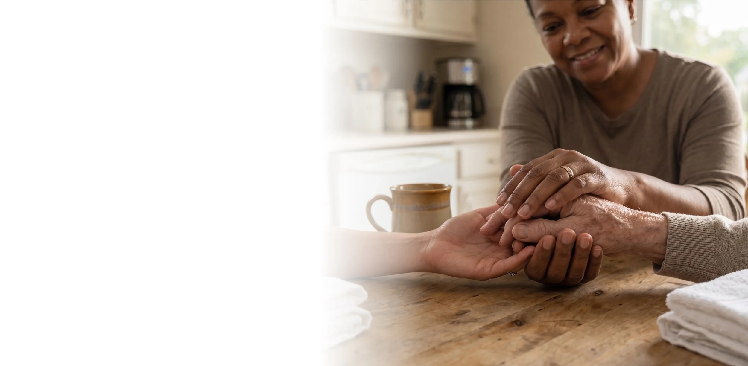 Close-up of a person gently holding an elderly woman's hands in a comforting gesture.