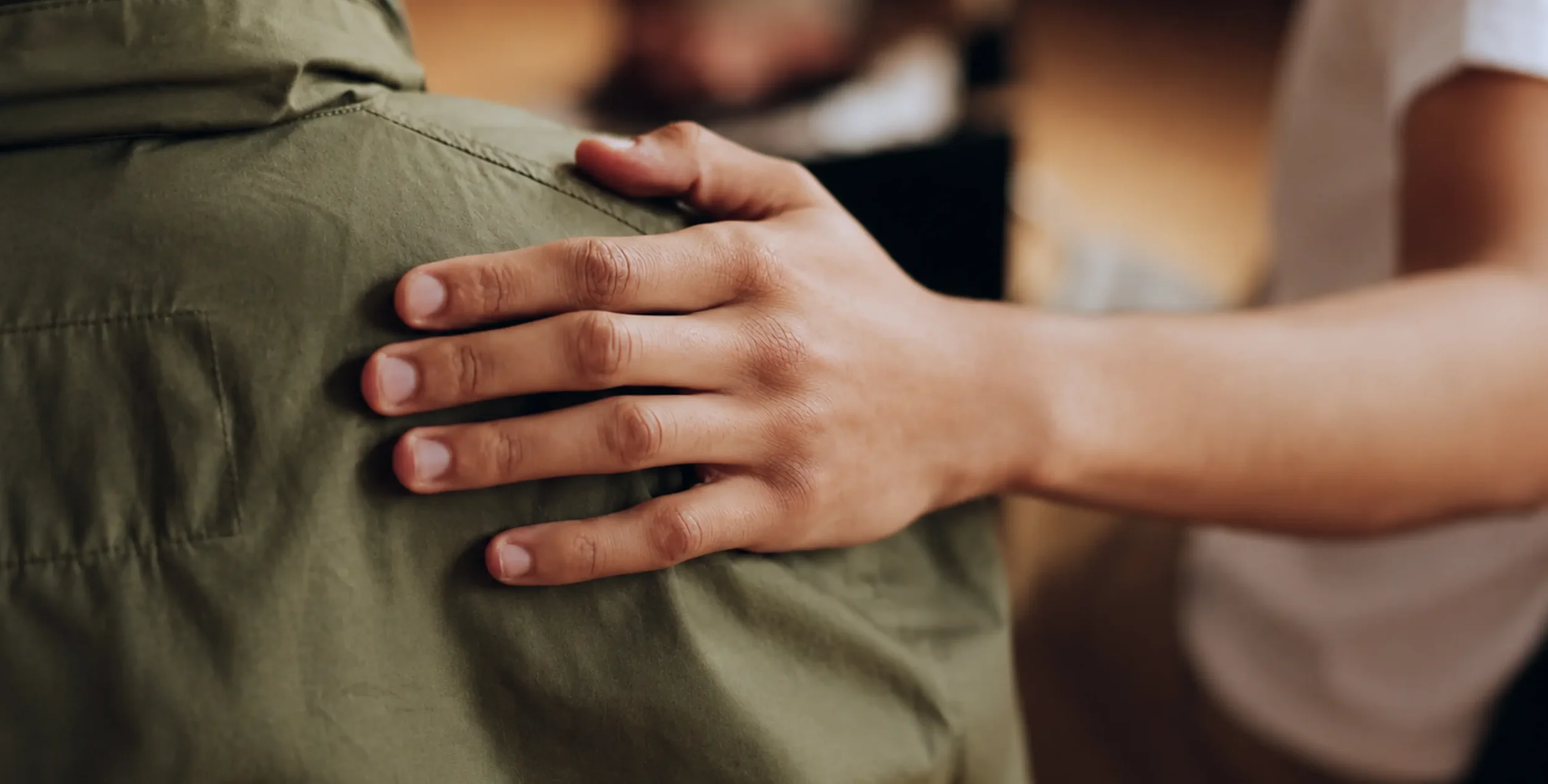 Close-up of a hand placed gently on another person's back in a gesture of care and support.