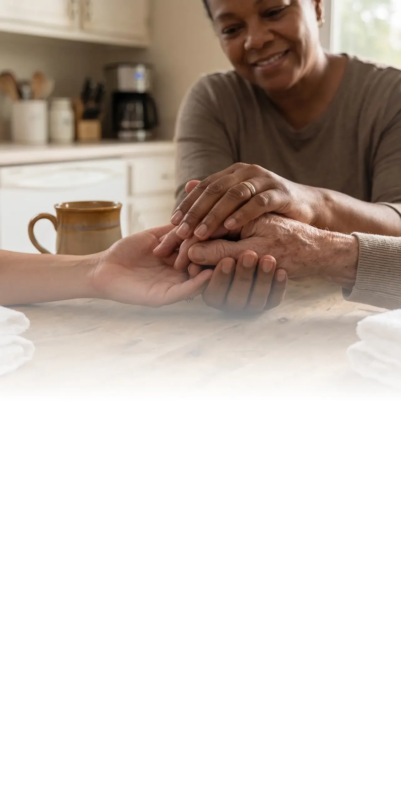 Close-up of a person gently holding an elderly woman's hands in a comforting gesture.
