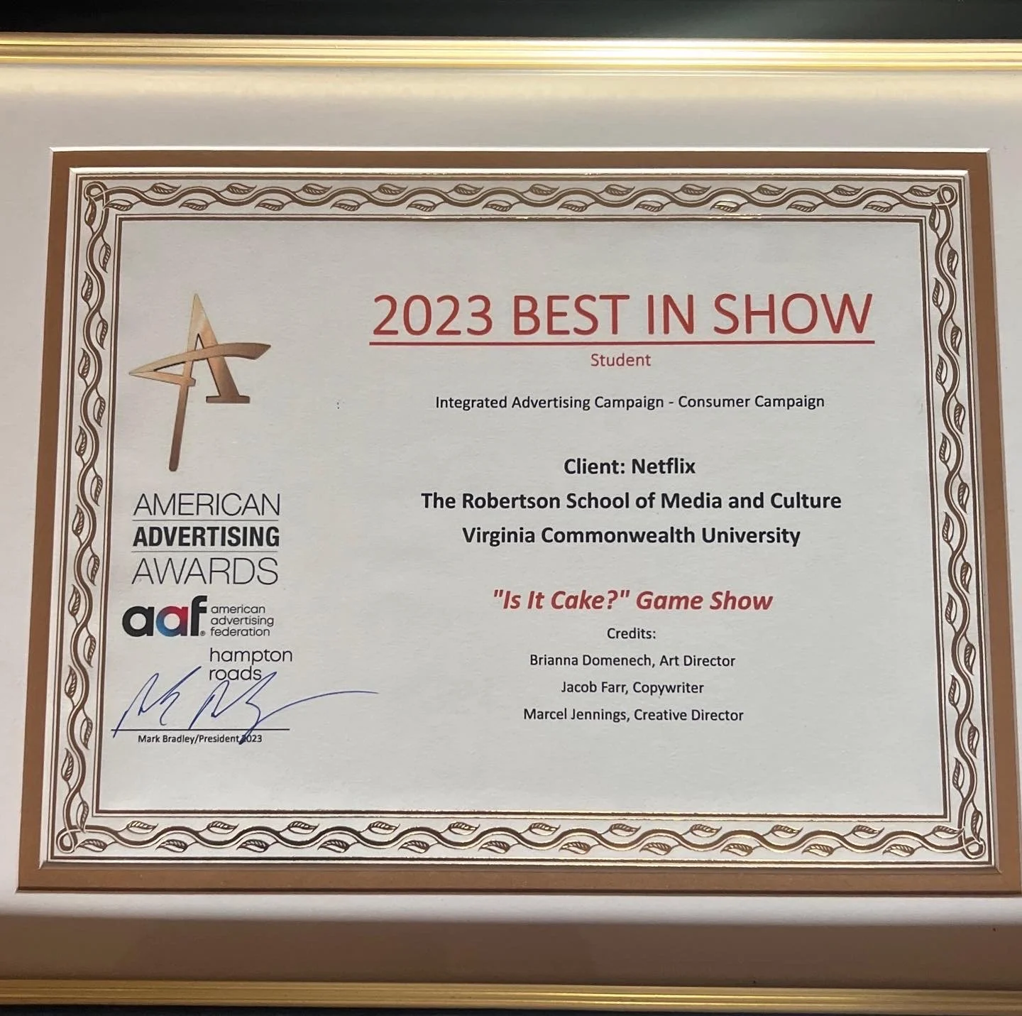 Certificate of award titled '2023 Best in Show' awarded to student for an integrated advertising campaign for Netflix called 'Is It Cake?' Game Show, from the American Advertising Awards, signed by Mark Bradley, president, and noting credits for Brianna Domenech, Jacob Farr, and Marcel Jennings, with the logo of American Advertising Federation and Hampton Roads.