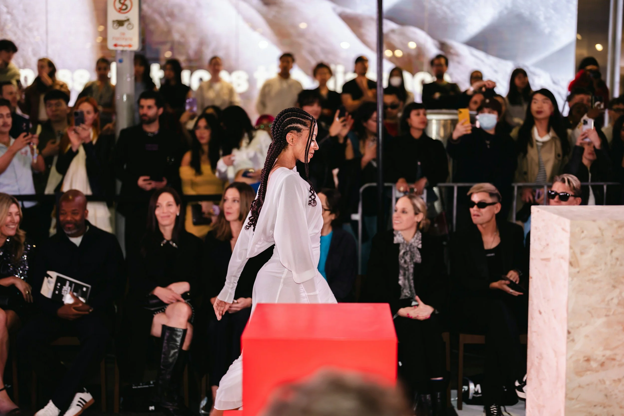 A woman walking down a runway at a fashion show with an audience watching and taking pictures.