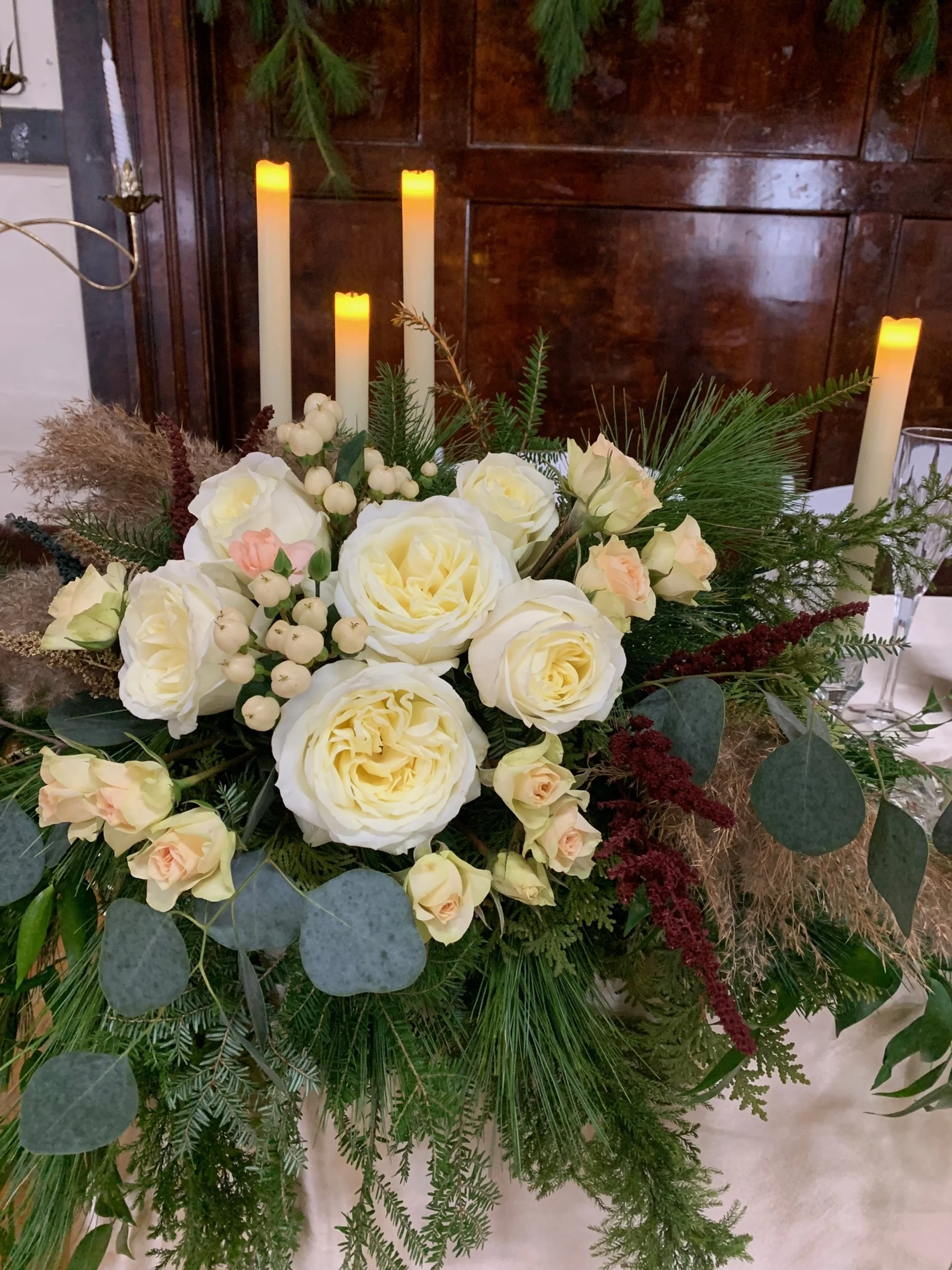 white roses winter greenery and candles arrangement