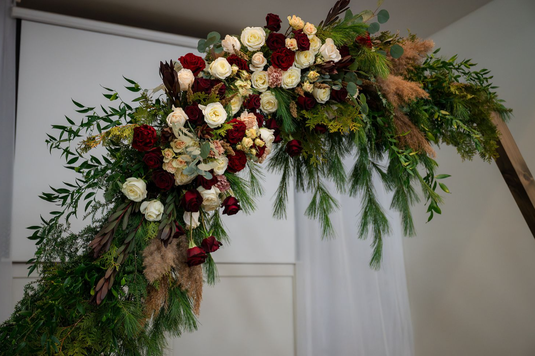 lush floral arch with winter greenery, white and red roses