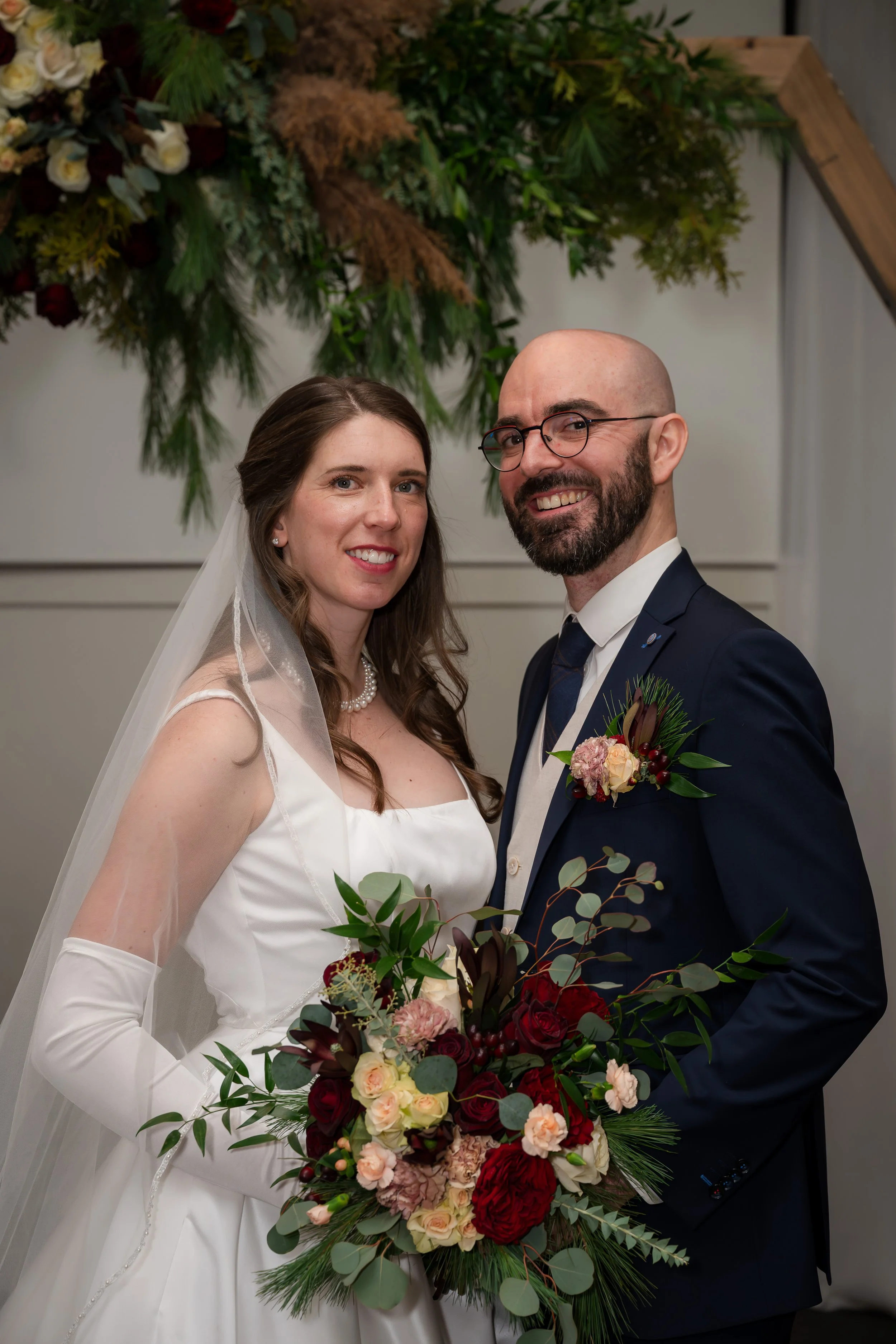 bride and groom holding bouquet and standing under wedding arch
