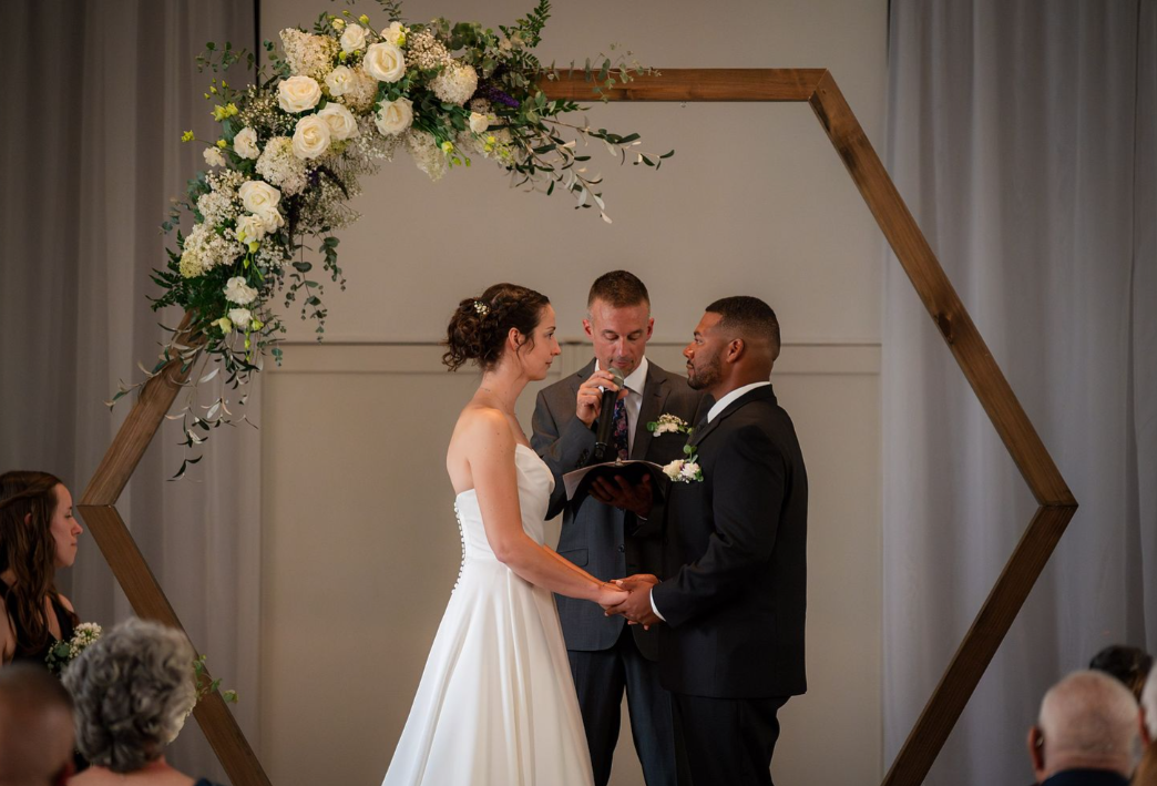 bride and groom under white floral arch swag