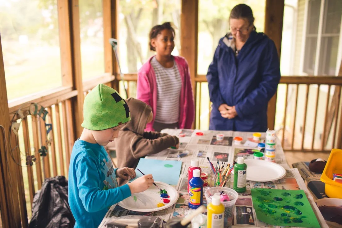 Children doing a painting activity on an outdoor balcony, supervised by an adult.