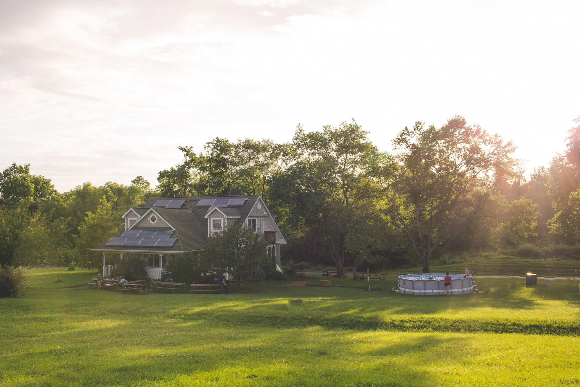 A wide grassy area leads up to one of the community homes. Picnic benches and an above ground pool are outside.