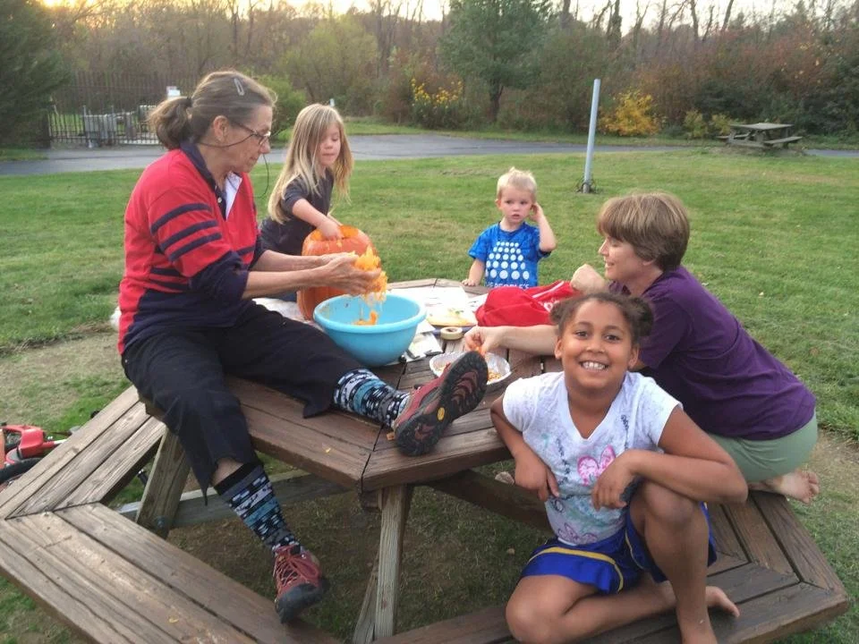 Children and an adult sitting at a picnic table pulling out pumpkin seeds from a pumpkin.