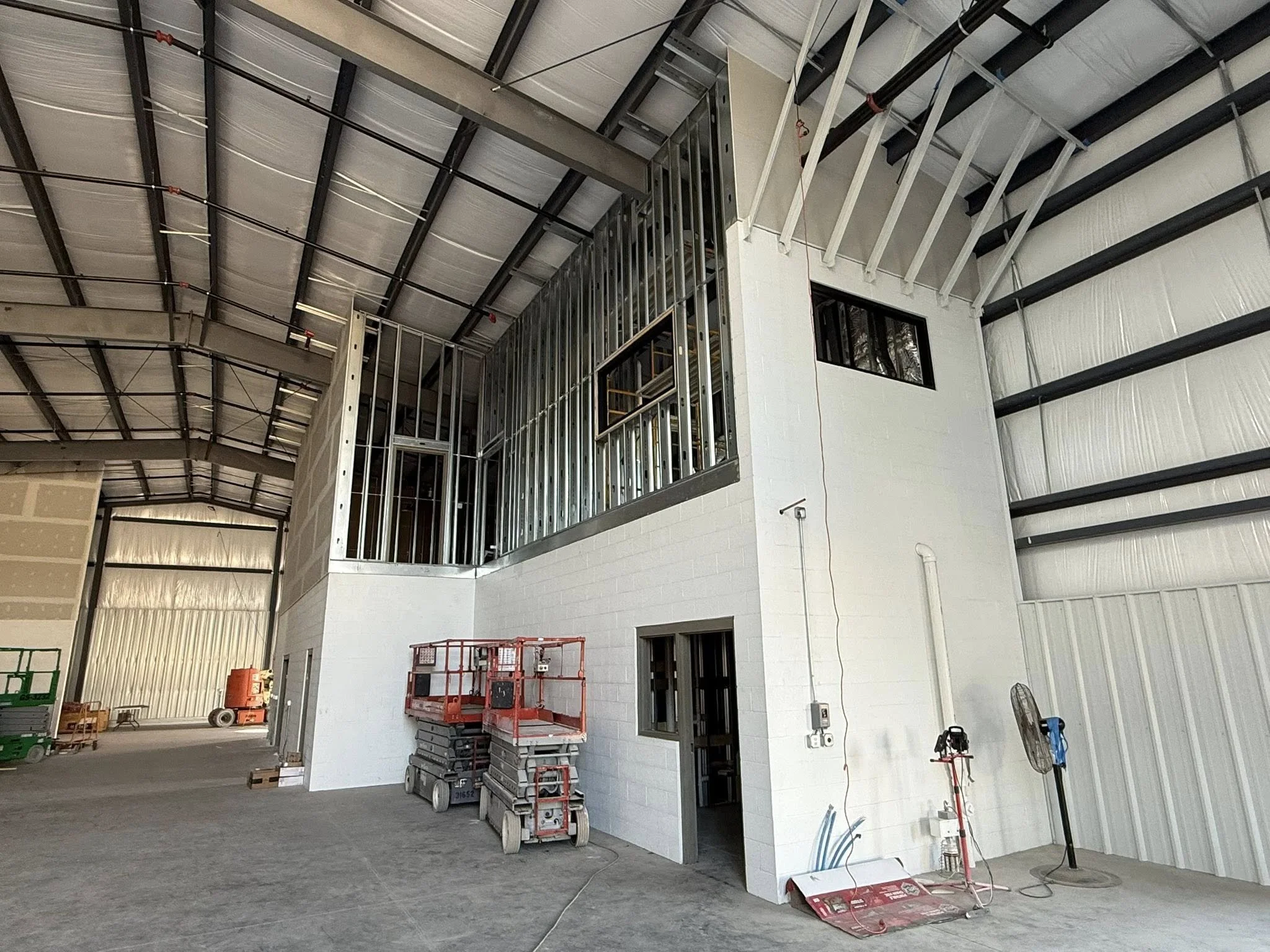 Interior of a warehouse under construction with metal framing, a scissor lift, and construction tools.