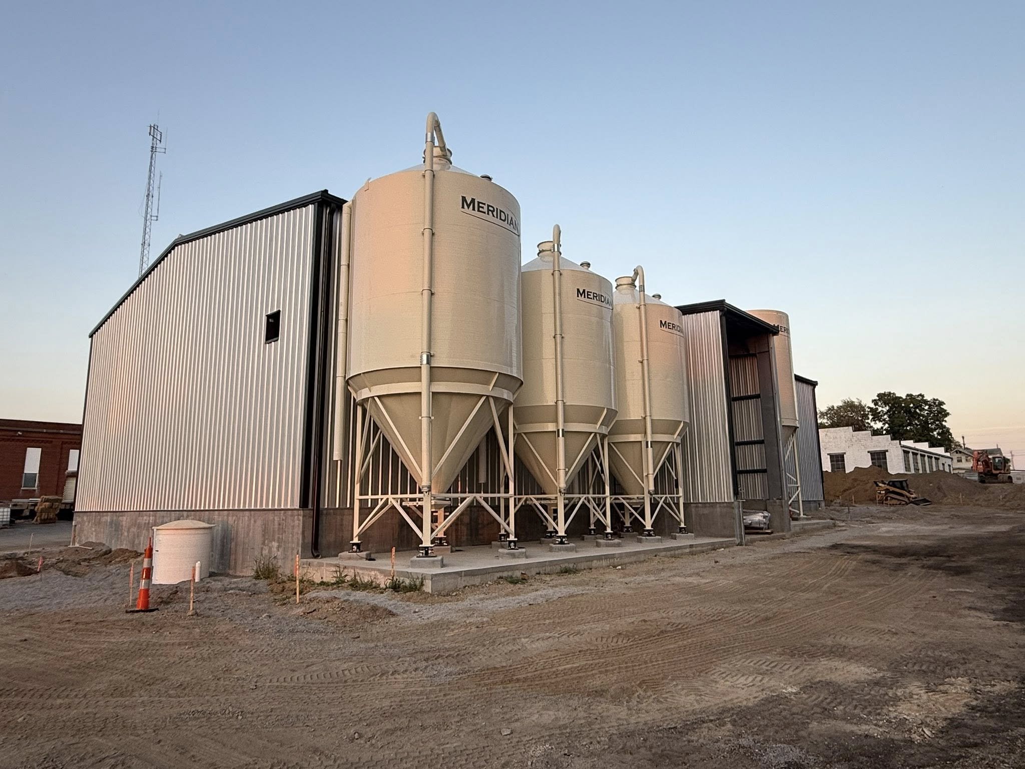Industrial grain silos and storage tanks at a construction site during dusk.