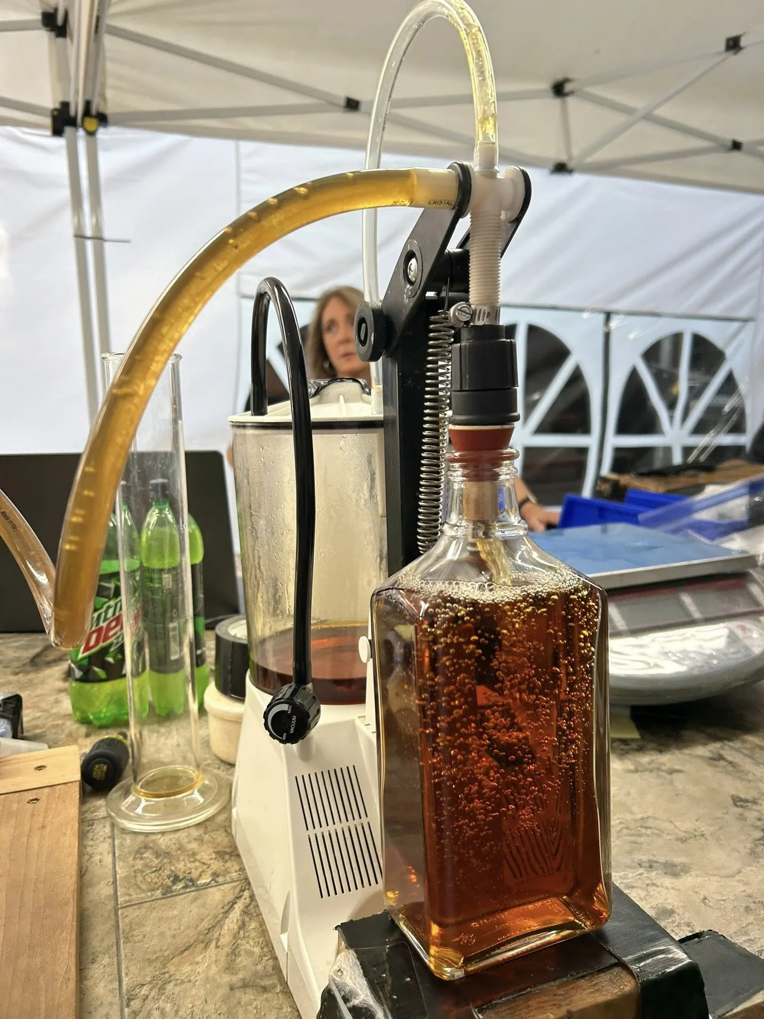 A laboratory setup with a distillation apparatus on a table, including a boiling flask with amber liquid, connected to a condenser, with a woman in the background.